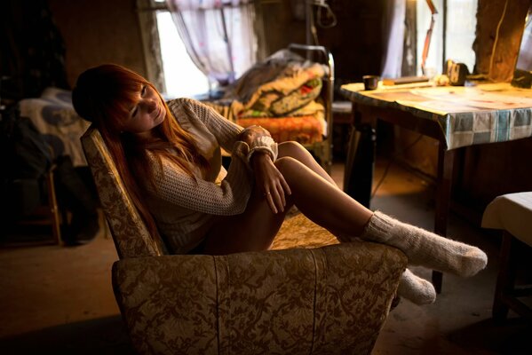 A red-haired girl is sitting in a room in an armchair