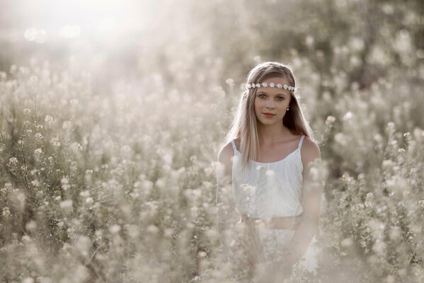 A girl in white with a wreath on her head is sitting in the grass