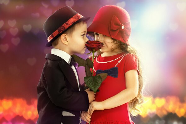 Мальчки и девочка в шляпах нюхают розу