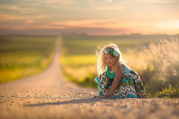 Niña en vestido sentado en la carretera