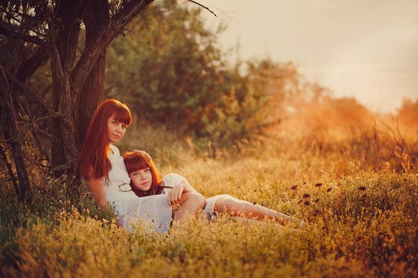 Madre e hija como gemelas bajo un árbol en la naturaleza