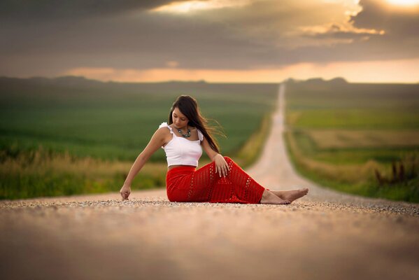 Chica en falda roja se sienta en la carretera