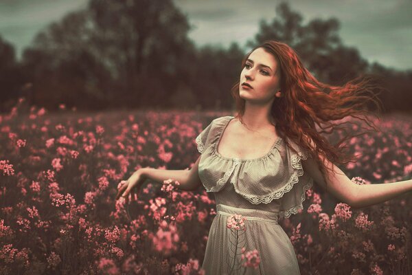 Chica de pelo rojo con rizos en el campo con flores