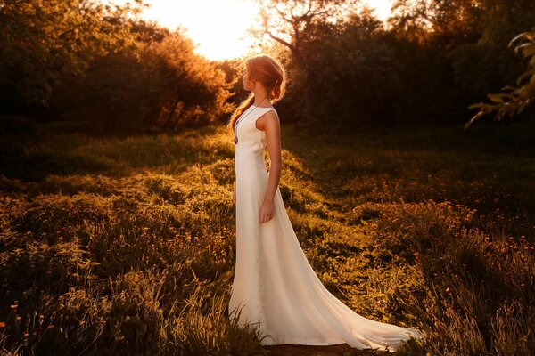 La jeune fille dans une robe blanche au coucher du soleil