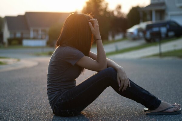 The girl is sitting on the asphalt with her back turned