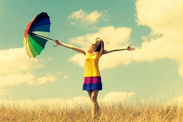 A girl in a field with a multicolored umbrella