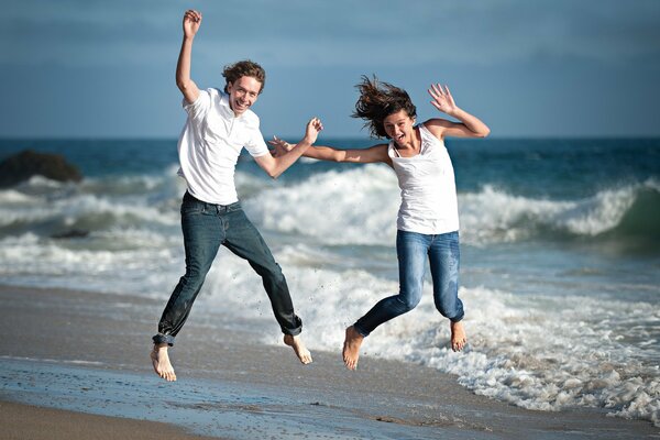 Fille avec un mec sur le sable près de la mer sautant de bonheur