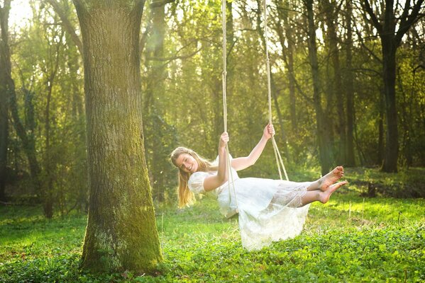 Mädchen im weißen Kleid auf einer Schaukel im Wald