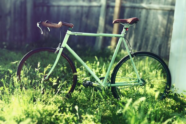 Turquoise bicycle fix on the grass on the background of the fence