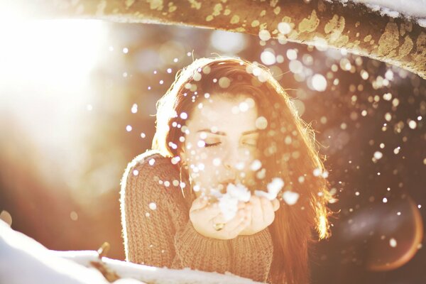 Beautiful girl blowing on snowflakes in her palms