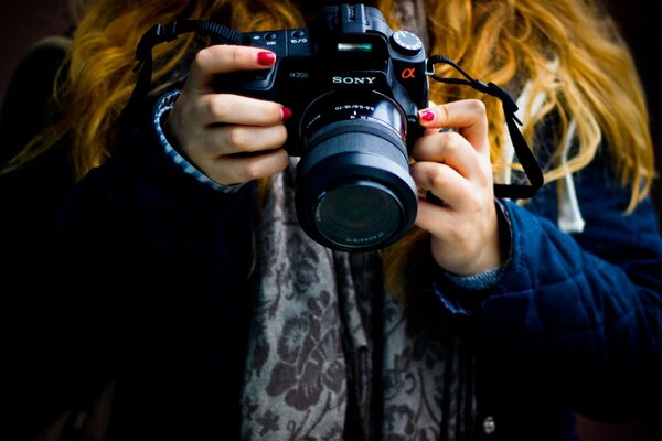 Fille aux cheveux roux et vernis rouge sur les ongles tient l appareil photo