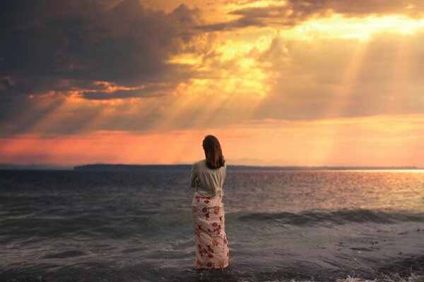 Chica en falda larga viendo la puesta de sol en el mar