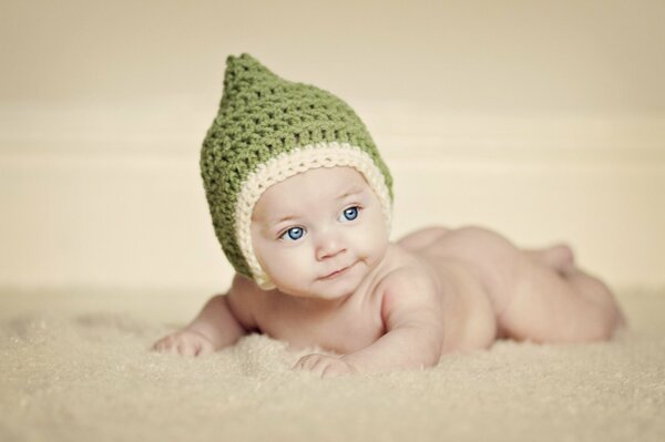 A baby in a knitted green hat is lying on his stomach