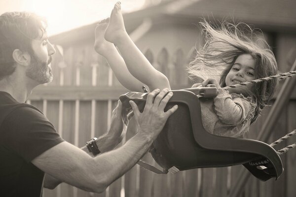 A man rides a little girl on a swing