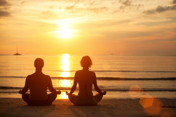 Мужчина и женщина медитируют на закате у моря