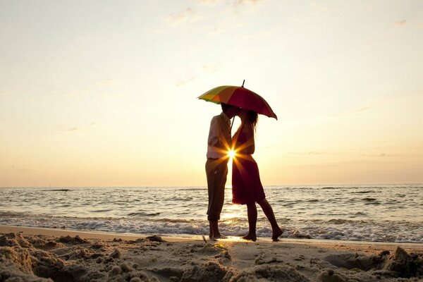 Amantes en el fondo de la puesta de sol en el mar con un paraguas en la mano