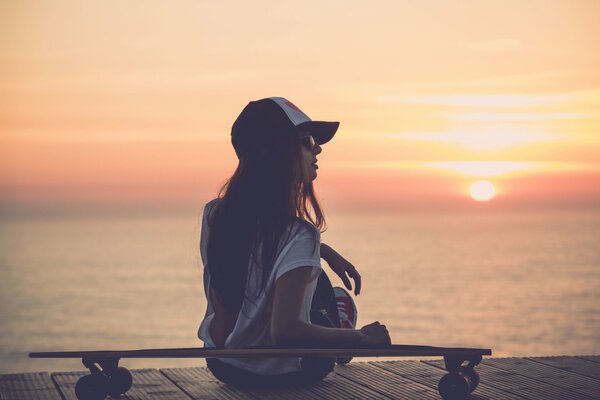 Jeune fille dans une casquette au bord de la mer au coucher du soleil