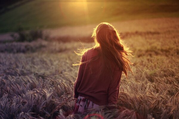 A girl in a wheat field in the rays of the setting sun