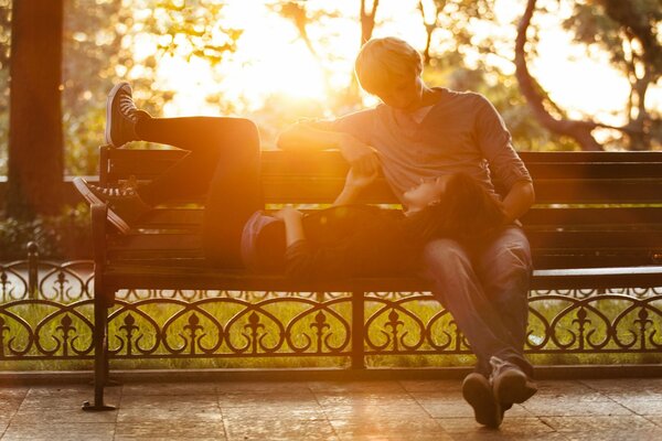 Homme et couché sur un banc femme couple amoureux chaud razovor dans la nature pendant la journée sur fond d arbres et le soleil