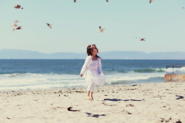 Baby in white on the beach with seagulls