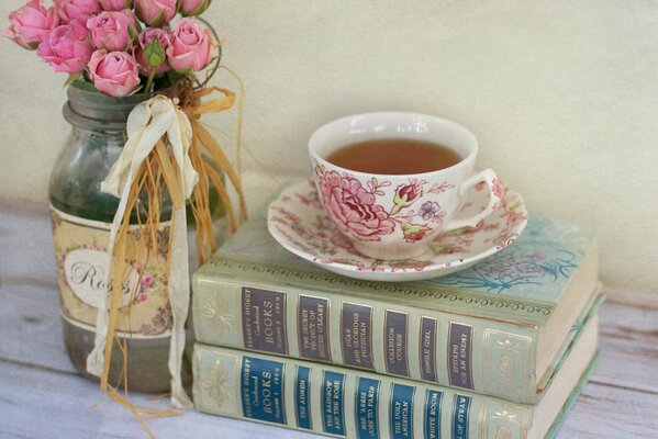 Ein Strauß rosa Rosen in einem Glas und Bücher liegen nebeneinander mit einer Tasse Tee