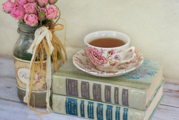 Mazzo di rose rosa in un barattolo e libri accanto con una tazza di tè