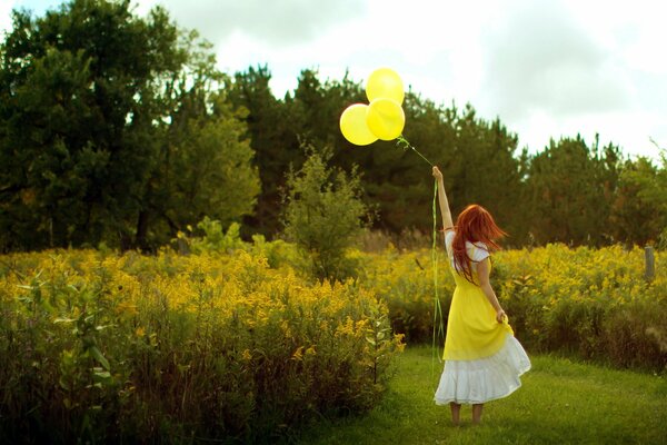 Ragazza rossa in un vestito bianco-giallo con le palle gialle sul pavimento con gli alti fiori gialli