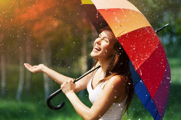 A girl with a multicolored umbrella rejoices in the rain