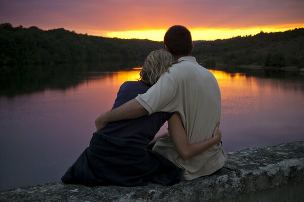 Los amantes observan la puesta de sol en el lago