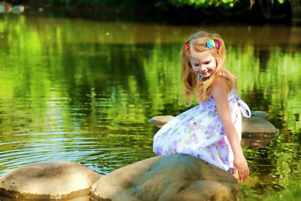 In the hot summer, it s nice to sit on a pebble by the lake, even if you re a little girl