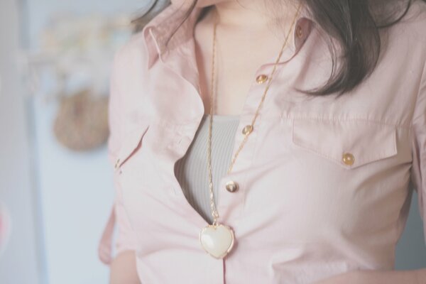 Una chica con una blusa rosa claro. Colgante en forma de corazón