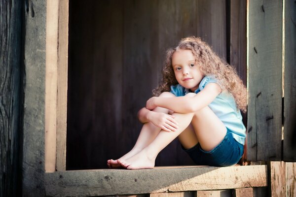 Chica con el pelo rizado sentado en el porche