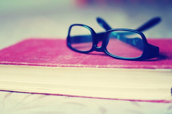 Brille mit schwarzem Rand auf einem leuchtend rosa Buch