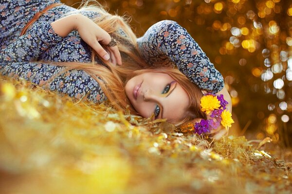 Una chica con un vestido abigarrado y flores en el pelo yace entre las hojas de otoño