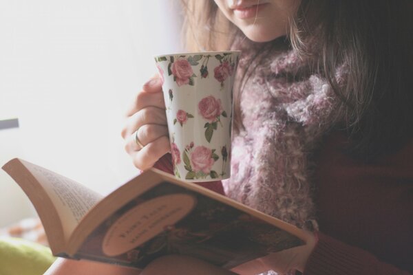 A girl in a sweater reads a book and drinks tea