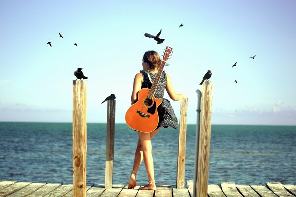 Una chica con una guitarra está en la orilla del mar