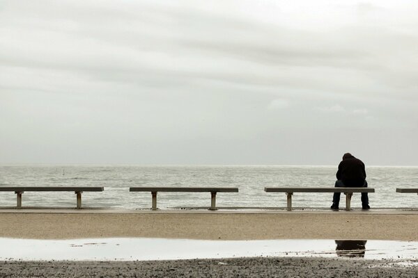 A lonely man in black is sitting on a bench by the sea