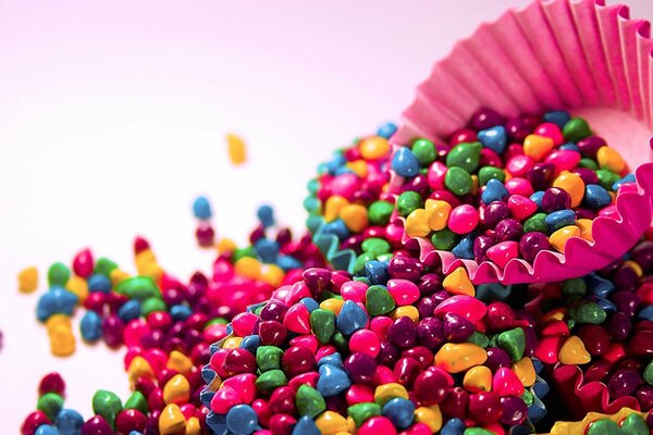 Multicolored candies are piled up by a pink paper capsule