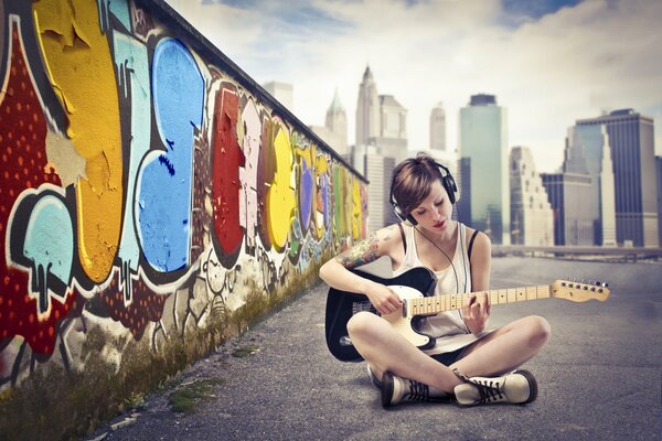 Ragazza in cuffia contro il muro con graffiti che suona la chitarra