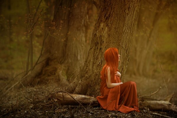 A red-haired girl is sitting in the forest