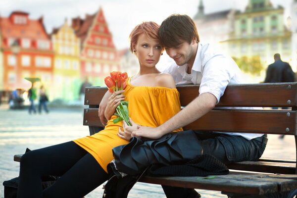 A red-haired girl in a yellow dress with tulips in her hands on a bench