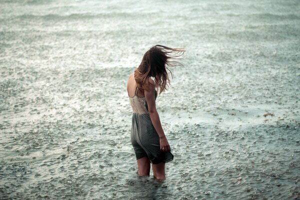 A lonely girl is knee-deep in water standing under a torrential