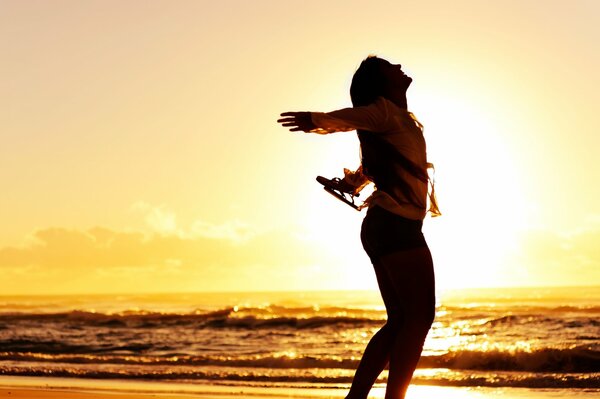 Silhouette of a joyful girl against the background of a sea sunset