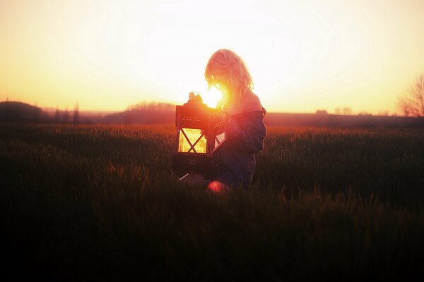 A girl in a field with a lamp at sunset