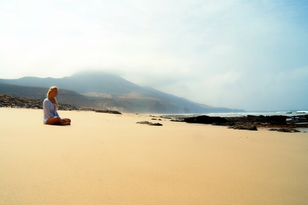 A girl is sitting alone on a sandy beach