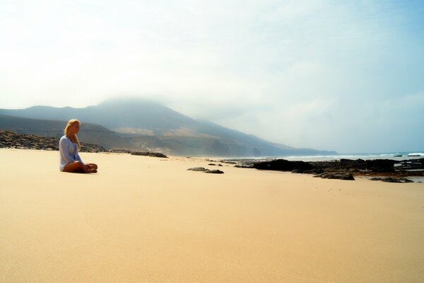 Девушка сидит одна на песчаном пляже
