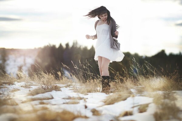 Mädchen in Kleid und Stiefeln im Feld mit geschmolzenem Schnee Frühling