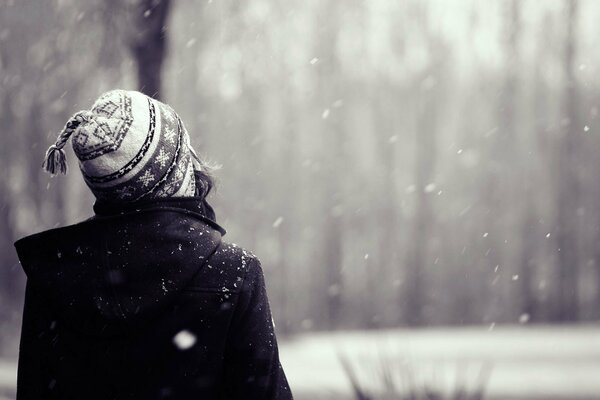 A girl in a hat looks at the falling snow