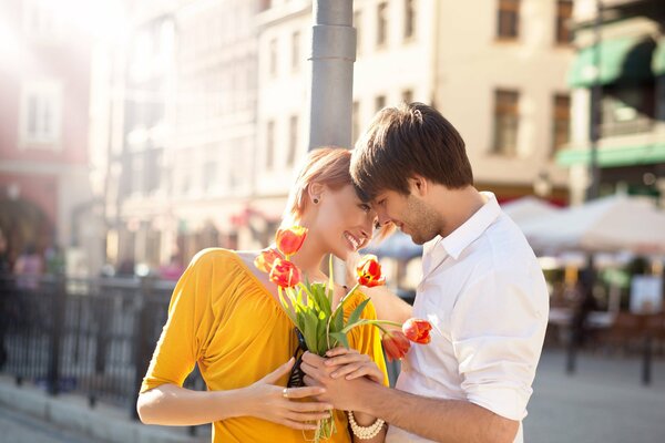 Chica y chico en una cita romántica en un día soleado en la ciudad con un ramo de tulipanes rojos