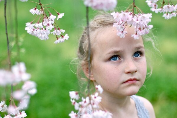 Грустная маленькая девочка в цветущем саду